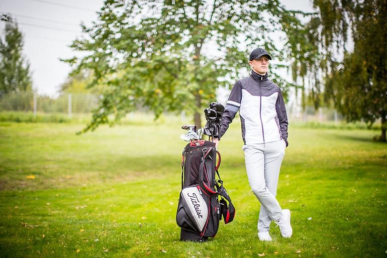 Avslappnad golfare står lutad mot sin golfbag.