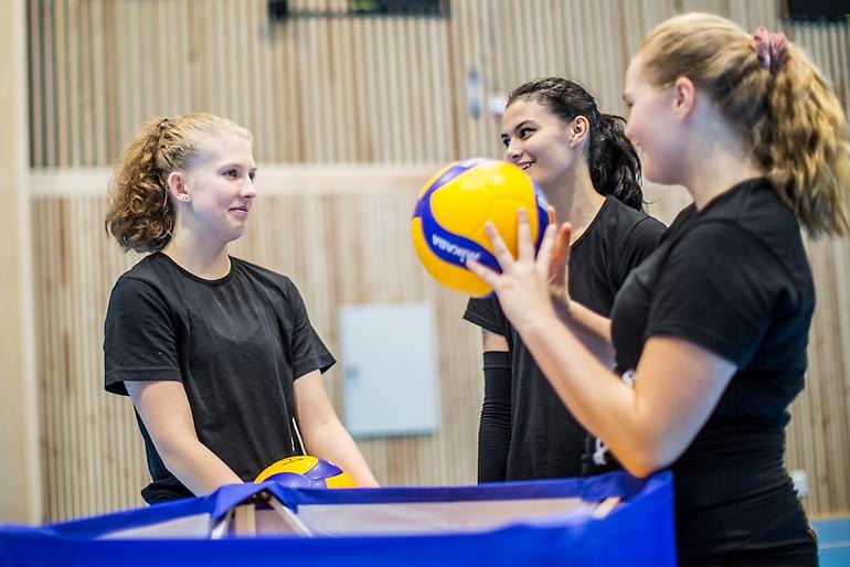 Unga volleybollspelare småpratar vid bollvagnen.