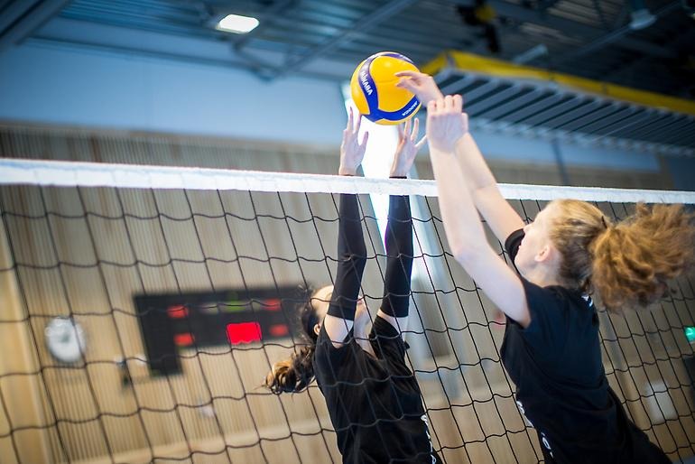 Två volleybollspelare i full action framme vid nät.